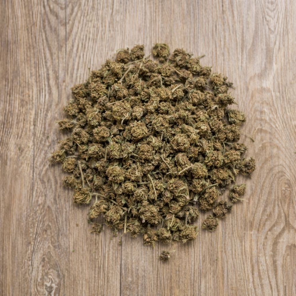 Tas de petites fleurs CBD OG Kush en vrac pose sur surface en bois.