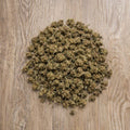 Tas de petites fleurs CBD OG Kush en vrac pose sur surface en bois.