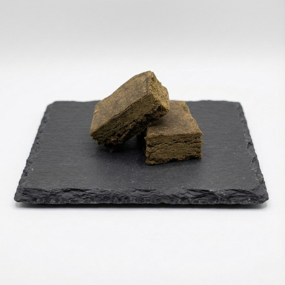 Deux blocs de hash CBD poses sur ardoise noire avec fond blanc.