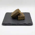 Deux blocs de hash CBD poses sur ardoise noire avec fond blanc.