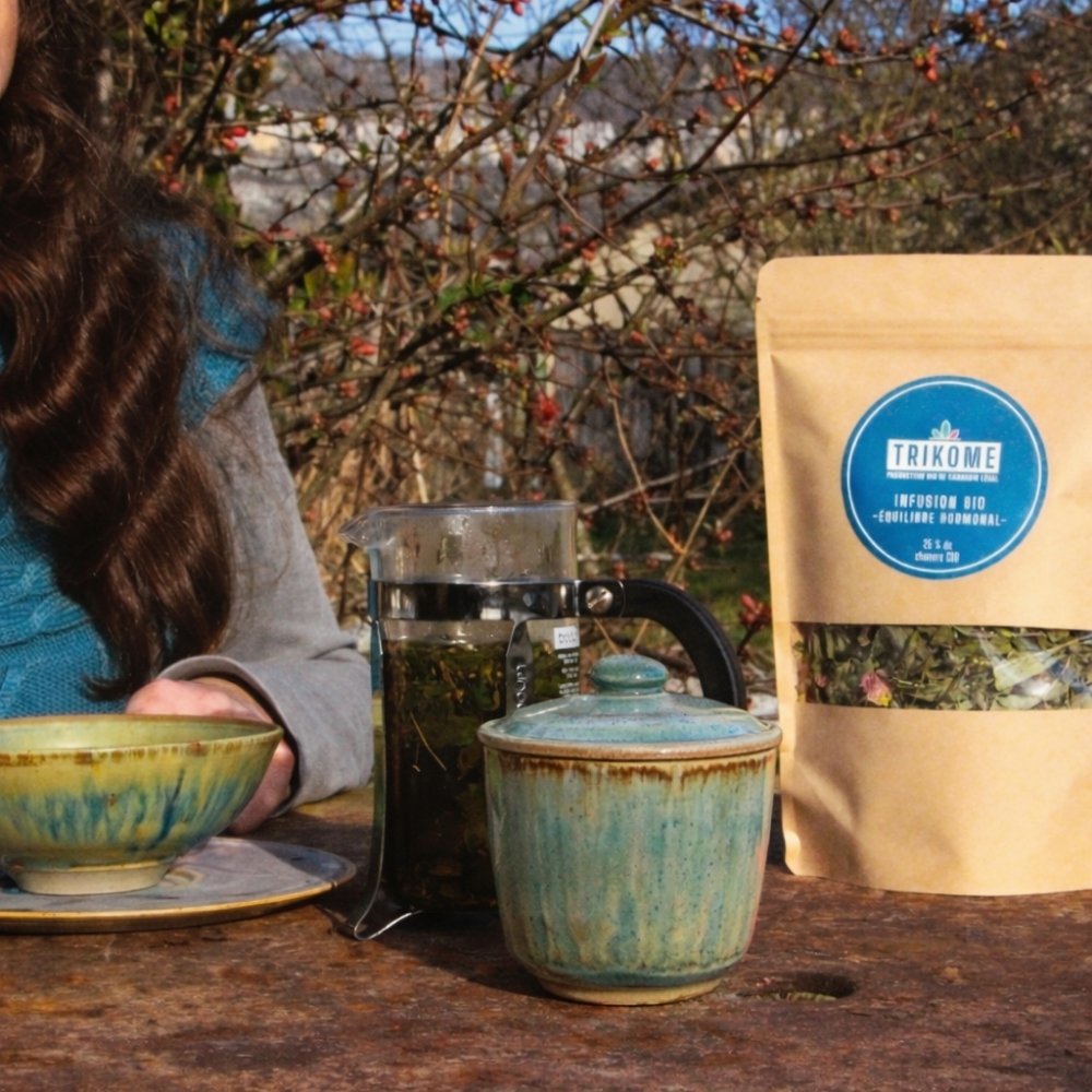 Tasse emaillee rouge avec couvercle posee en exterieur pres d une riviere pour illustrer un moment infusion nature